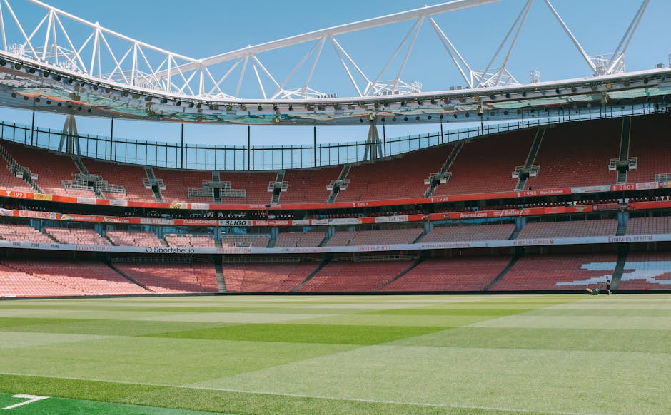 There is no image of flowers or floral arrangements; instead, the image depicts a large, empty football stadium with a well-maintained green pitch, red seating sections, and a partial view of the roof