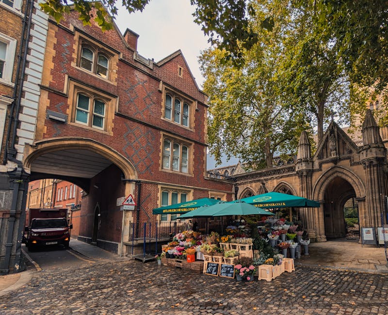 A flower stall set up outdoors on a cobblestone street, featuring a variety of fresh flowers including roses, tulips, and chrysanthemums in bright colors such as pink, yellow, and white. The flowers a